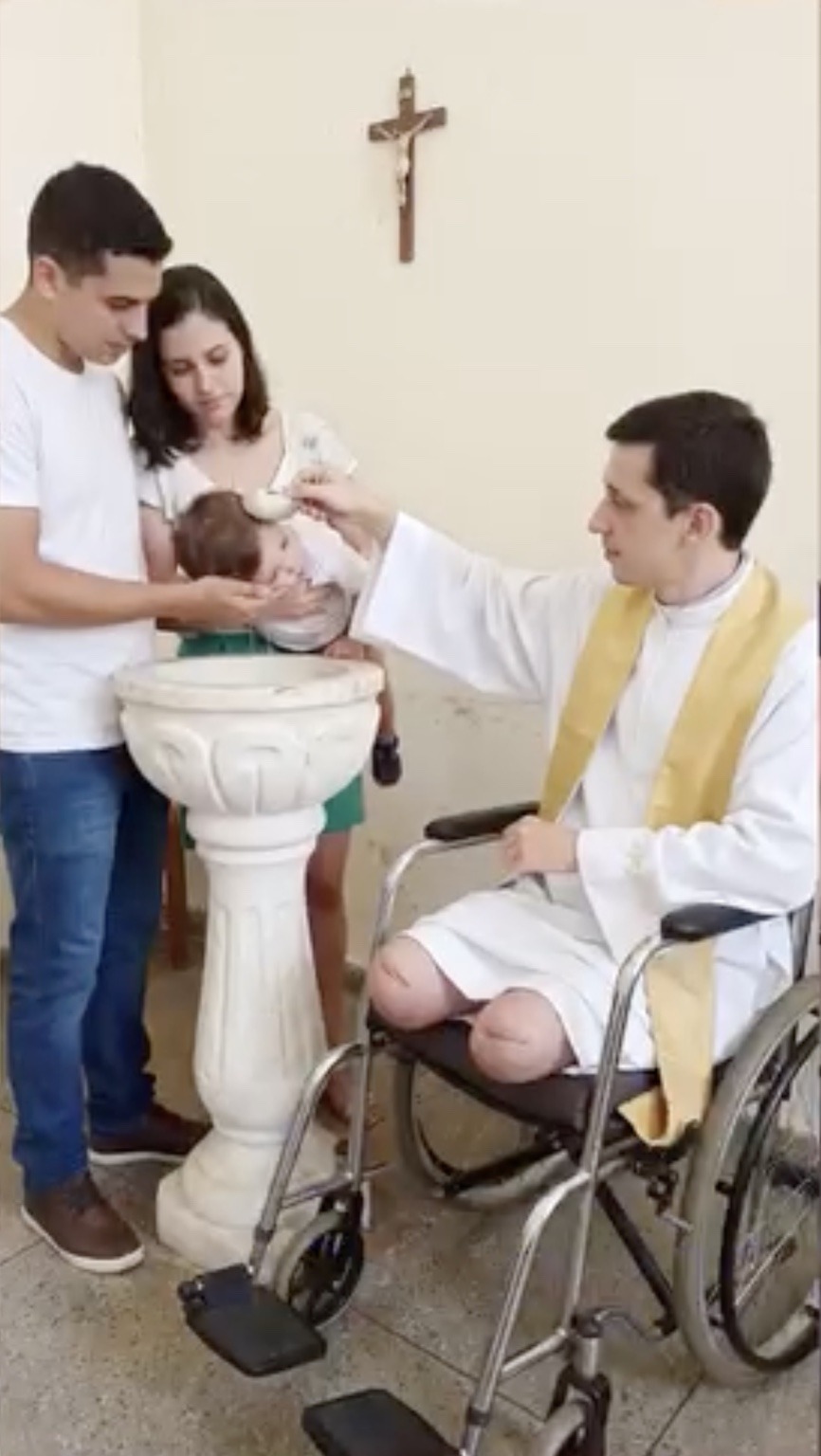 Padre Miguel realizando un bautismo sentado en su silla de ruedas